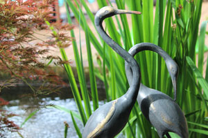 Photo of elegant iron cranes standing alongside koi pond and irises